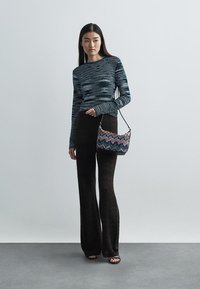 Πλεκτή μπλούζα με μακριά μανίκια σε μπλε και λευκές ρίγες, συνδυασμένη με σκούρες καφέ παντελόνες σε φαρδιά γραμμή με σχέδιο και μια πολύχρωμη τσάντα σε ζιγκ-ζαγκ.