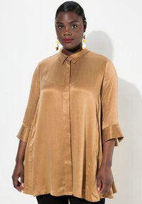 Blusa satinata color marrone chiaro con colletto, maniche a tre quarti e vestibilità morbida. Presenta una trama a righe sottili e una chiusura con bottoni.