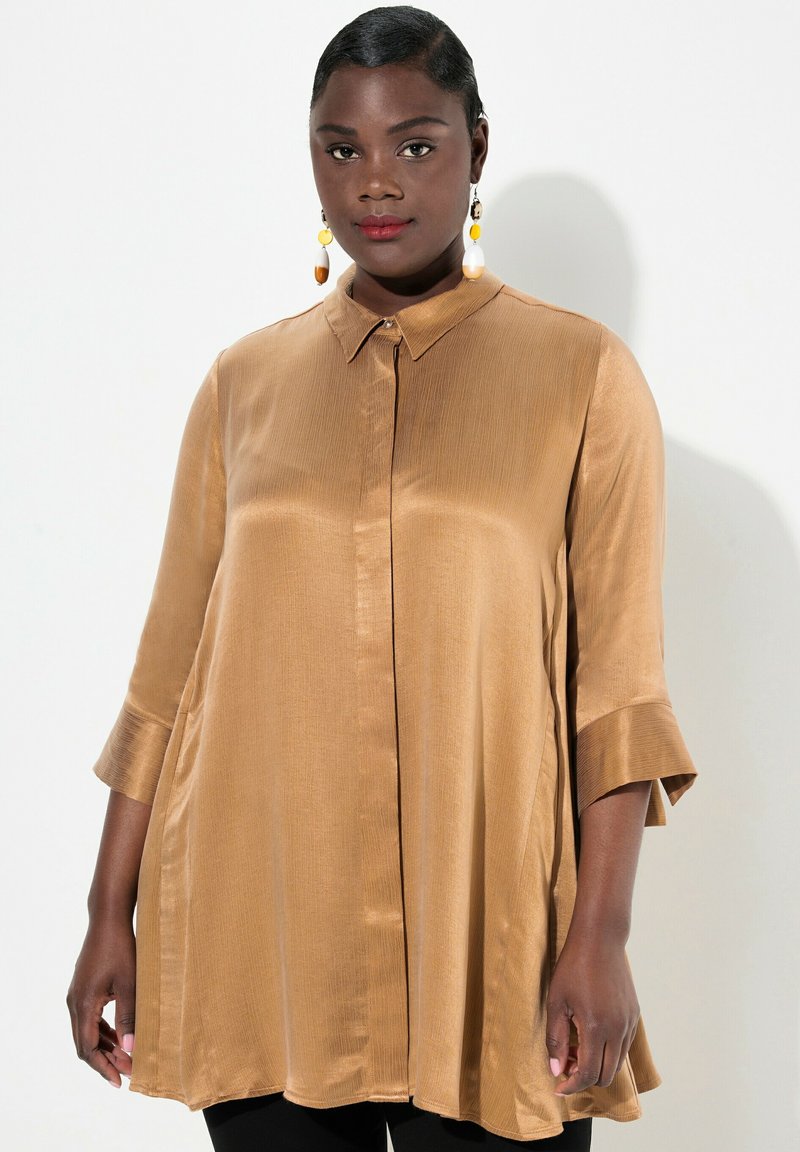 Blusa satinata color marrone chiaro con colletto, maniche a tre quarti e vestibilità morbida. Presenta una trama a righe sottili e una chiusura con bottoni.