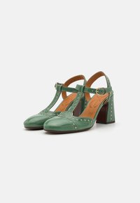 Green leather T-strap heels with perforated detailing, rounded toe, chunky heel, and buckle closure on the ankle strap.