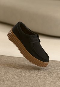 Svart sko med en glatt overdel, snøring og en teksturert, brun gummisåle med uttalte spor.