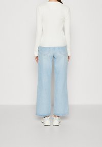 Vit ribbad långärmad topp, kombinerad med ljusblå vida jeans och vita sneakers. Enkel design med en figurnära silhuett och ärmslut.