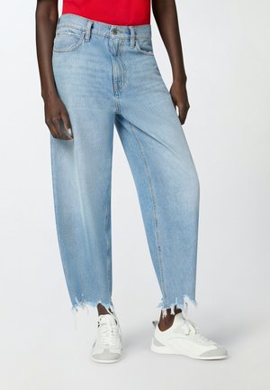 Jeans azzurri chiari con taglio rilassato e orlo sfrangiato, design a cinque tasche e passanti per cintura, abbinati a sneaker bianche da ginnastica.