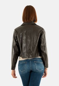 Giubbotto in pelle grigio scuro, tagliato, con collo e polsini a bottoni, abbinato a jeans blu con un motivo delicato sulle tasche posteriori.