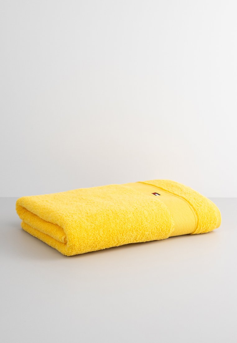 Serviette jaune vif pliée avec un petit logo rectangulaire sur une surface et un fond clairs.
