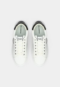 Ett par vita låga sneakers med svarta hälakcenter, vita snören och "KARL LAGERFELD"-logotyp på tungan och innersulan.
