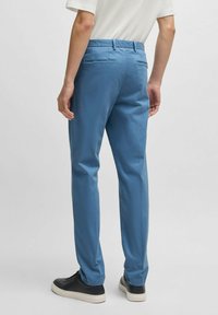 Light blue trousers with a straight-leg design, featuring back pockets and a smooth cotton fabric texture. Worn with black sneakers.