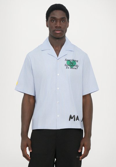 Camicia a maniche corte a righe azzurre, con chiusura a bottone, caratterizzata da stampe di testo verdi e nere sul petto e sull'orlo. Realizzata in un tessuto liscio.