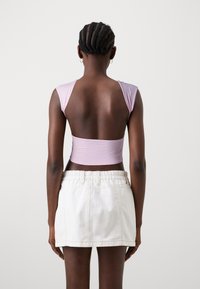 Top cropped lilla con spalle larghe e schiena scoperta, abbinato a una gonna di jeans bianca con vita arricciata e lunghezza corta.