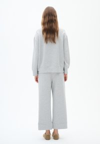 Grijze sweatshirt met een losse fit en afhangende schouders, gecombineerd met grijze wijde broek, beide gemaakt van zacht materiaal. Model draagt pluizige slippers.