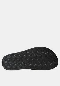 Black rubber shoe sole with a geometric tread pattern featuring hexagonal shapes and a logo imprint, offering textured grip and durability.