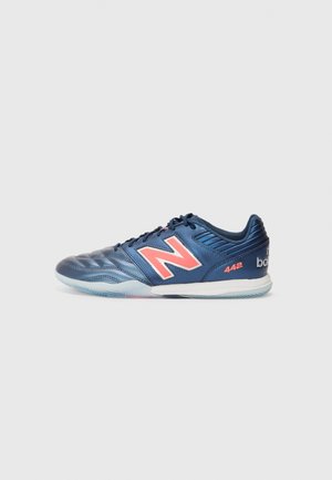 Blue athletic shoes with a textured synthetic upper, featuring a prominent pink "N" logo, lace closure, and a light blue rubber outsole.