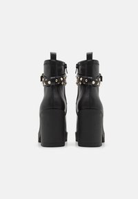 Botine negre din piele, cu toc gros, embellisite cu curele cu capse. Au închidere cu fermoar și accente texturate.