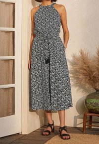 Robe à col halter avec un motif géométrique noir et blanc, cintrée à la taille par un cordon, affichant une silhouette évasée fluide et des poches latérales.