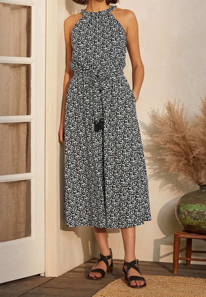 Robe à col halter avec un motif géométrique noir et blanc, cintrée à la taille par un cordon, affichant une silhouette évasée fluide et des poches latérales.