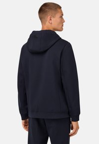 Temno moder kapucar s fitted obliko, z vrvico za nastavljanje kapuce in rebrastimi manšetami. Gladka tkanina iz bombažnega mešanica, z diskreto oznako na hrbtni strani.