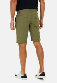 Olijfgroene shorts met een rechte snit, voorzien van details op de achterzakken en een nette zoom, gecombineerd met witte en donkerblauwe sneakers.