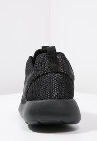 Svart mesh träningsskor med en texturerad yta, vadderad krage och en formgjuten svart gummisula. Har en dragflik bak.
