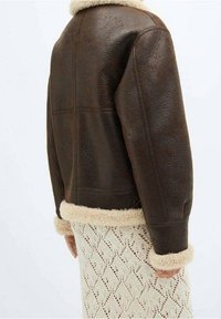 Veste en cuir marron avec un col et des poignets en shearling beige doux, présentant une finition texturée et un design court.