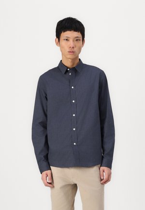 Dark blue, long-sleeved, button-up shirt with a collar and white buttons. Fabric has a subtle texture, paired with light beige pants.