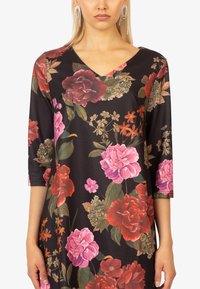Schwarzes Blumenkleid mit einem V-Ausschnitt und dreiviertel Ärmeln. Es zeigt große pinke und rote Rosen, grüne Blätter und eine sanfte Stofftextur.