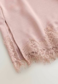Tissu rose doux avec une bordure en dentelle florale festonnée le long du bord et une petite fente latérale.