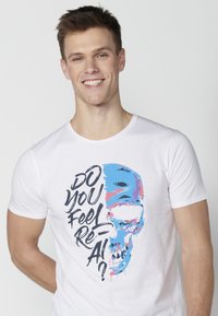 White cotton T-shirt featuring a colorful skull design with blue and pink accents and the text "DO YOU FEEL REAL?" in black lettering.