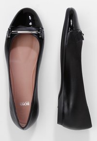 Czarne skórzane płaskie buty z błyszczącym czarnym lakierowanym noskiem, akcentem w postaci srebrnego hardware'u oraz gładką teksturowaną podeszwą.