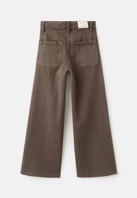 Pantaloni maro din denim cu croială largă și două buzunare în spate. Țesătură texturată cu margine nefinisată. Eticheta este vizibilă la talie.