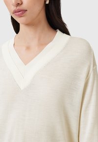 V-Ausschnitt Pullover in hellem Creme, weiche Textur, mit einem geschichteten Ausschnitt und subtilem Stichdetail. Schlichte, lockere Passform.