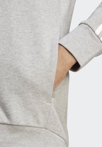 Pelēks sporta krekls ar ribotām aprocēm; satur kangaru kabatu; mīksta, teksturēta auduma; smalka stitcha detaļa sānos.