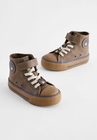 Braune High-Top-Schuhe aus Leder, mit einer braunen Gummizohle, cremefarbenen Schnürsenkeln und einem runden Aufnäher an der Seite. Gummisohle für Traktion.