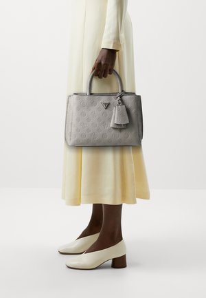 Borsa grigia con texture e motivi in rilievo, con doppio manico, un'etichetta staccabile e una forma rettangolare strutturata. Indossata con un vestito giallo.