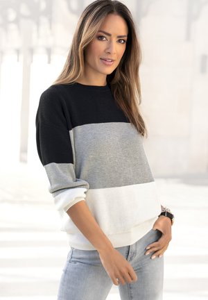 Strickpullover mit Farbblöcken in Schwarz, Grau und Weiß. Weit geschnittene Crew-Neckline und gerippte Bündchen mit weicher Textur. Kombiniert mit hellen Jeans.