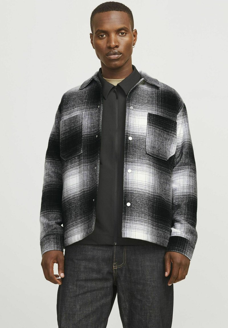 Black and white plaid shirt jacket in soft fabric, featuring two chest pockets, rounded collar, and button closure. Worn over a black top.