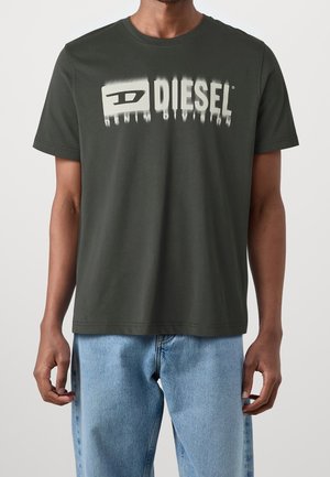 T-shirt en coton vert foncé avec un grand logo blanc "DIESEL" et le texte "DENIM DIVISION", col rond et manches courtes.