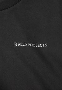 Camiseta negra con el texto "Rivvia PROJECTS" en blanco. Fabricada con tela suave y de textura lisa, con cuello redondo y corte holgado.