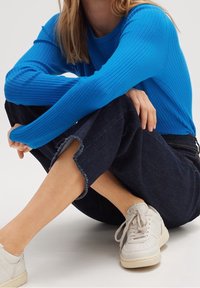 Blauwe geribbelde long-sleeve top, gecombineerd met donkere spijkerbroeken met rafelige zomen, aangevuld met witte sneakers met veters.