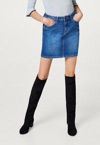 Falda de mezclilla con corte recto, color azul claro, dos bolsillos delanteros y cintura a media altura, combinada con botas de ante negras hasta la rodilla.