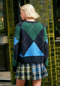 Sweter dzianinowy w zielono-niebiesko-czarny wzór argyle z różowymi przeszyciami. Dobrany do plisowanej spódnicy w kratę w odcieniach niebieskiego i zielonego.