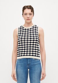 Strikket utenermed topp med bølgemønster i marineblått og kremfarge. Har rund halslinning og ribbestrikket kant. Kombinert med blå denimjeans.
