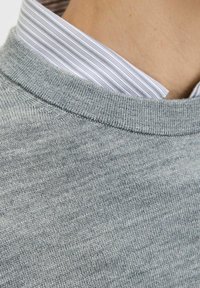 Szary sweter z dzianiny z teksturowanym kołnierzykiem, nałożony na kołnierzyk białej i szarej w paski koszuli pod spodem.