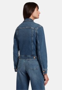 Giacca di jeans di blu medio con maniche lunghe, chiusura a bottoni e due tasche posteriori con design cucito. Texture liscia e forma aderente.