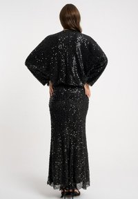 Czarna sukienka z cekinami o dopasowanym kroju, długich rękawach i rozkloszowanym dole. Teksturowana powierzchnia pokryta błyszczącymi cekinami.