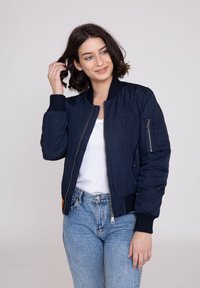 Marine bomberjakke med ribbede manchetter og krave, med lynlås foran og sidelomme. Stoffet ser glat og let skinnende ud.