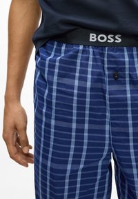 Pantaloni de lounge în carouri în albastru marin cu dungi albastre deschise. Talie elastică cu logo-ul "BOSS". Detaliu cu un singur nasture vizibil pe partea din față.