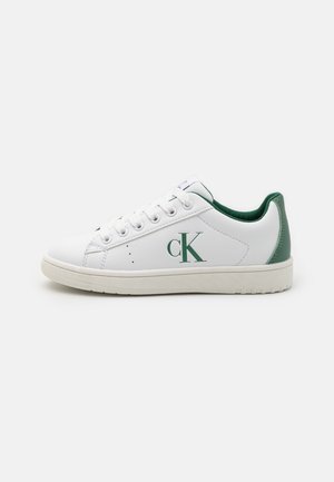 Baskets basses blanches avec accents verts, lacets et logo "cK" sur le côté, vues de l'extérieur sur un fond neutre.