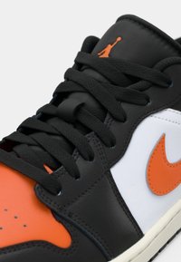 Gros plan sur une basket noire, blanche et orange avec des lacets noirs, un logo Nike swoosh orange et un logo Jumpman orange sur la languette.