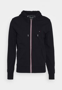 Sudadera con cremallera negra, con bolsillos frontales, cordones en la capucha y un pequeño logotipo rojo, blanco y azul en el lado izquierdo del pecho.