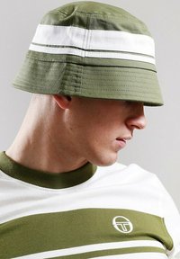 Cappello a secchiello verde e bianco con strisce orizzontali e tessuto strutturato, abbinato a una maglietta in maglia con scollatura rotonda e dettagli con logo.